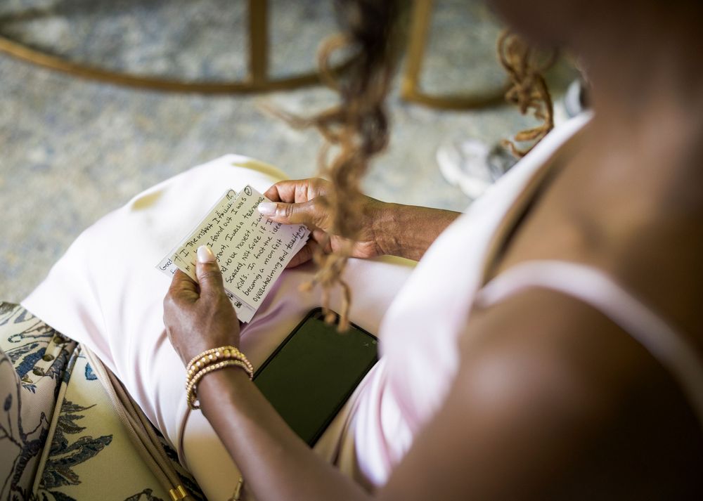 Bride in pink dress reads a heartfelt handwritten note while seated in a gold chair.