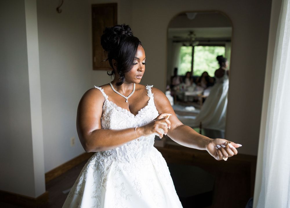 Beautiful Black bride in lace wedding gown adjusts her bracelet near a sunlit window.