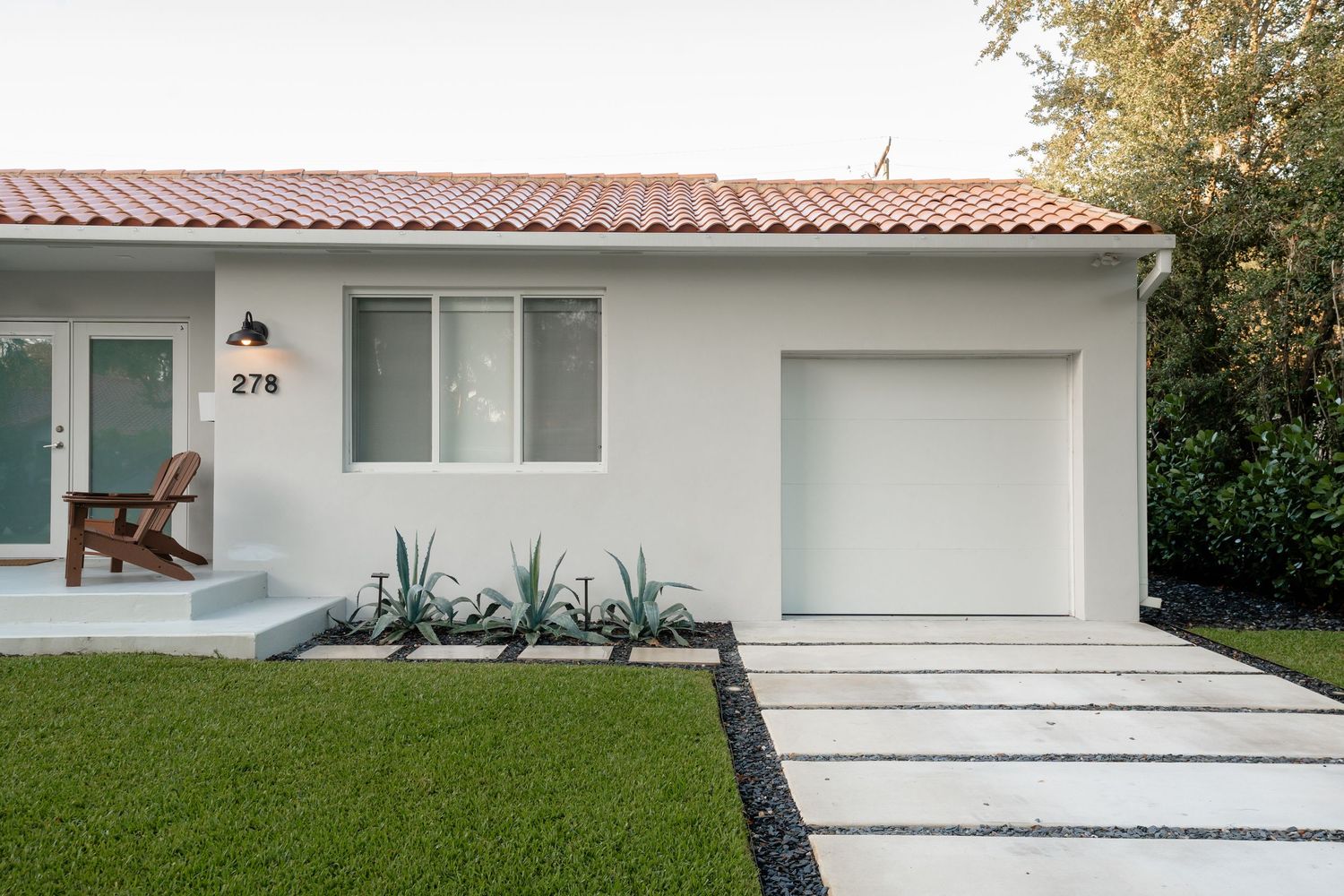 White stucco home with red tile roof, number 278, featuring a white garage door and modern landscaping with agave plants.