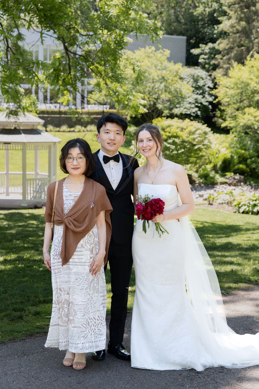 Bride and groom stand with grooms mother surrounded by greenery at the civic garden complex in london, ontario.