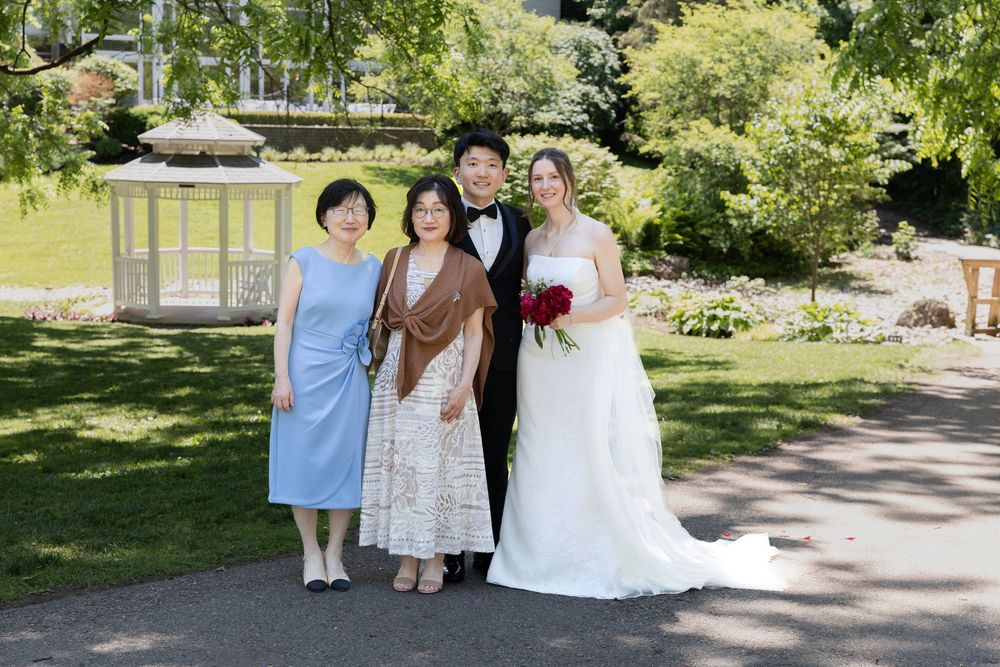 Bride and groom stand with grooms mom and sister surrounded by greenery at the civic garden complex in london, ontario.
