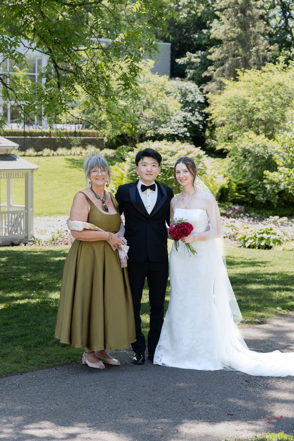 Bride and groom stand with brides mother surrounded by greenery at the civic garden complex in london, ontario.