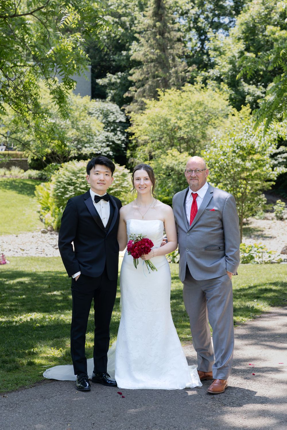 Bride and groom stand with brides father surrounded by greenery at the civic garden complex in london, ontario.