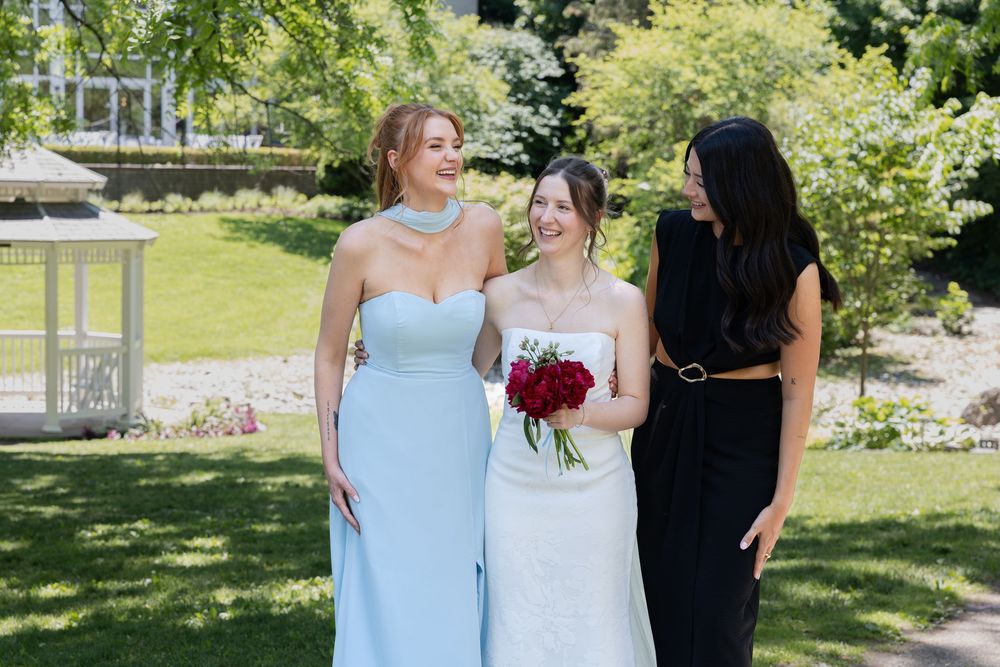 Bride laughs surrounded by bridesmaids surrounded by greenery at the civic garden complex in london, ontario.