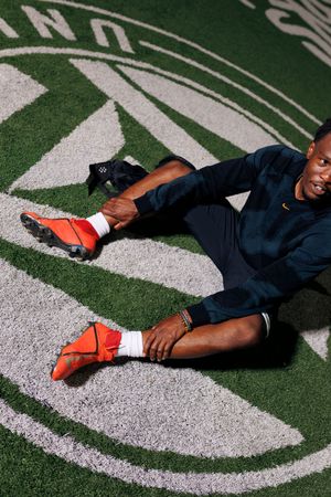 Soccer player in Nike red cleats stretching on green turf field.