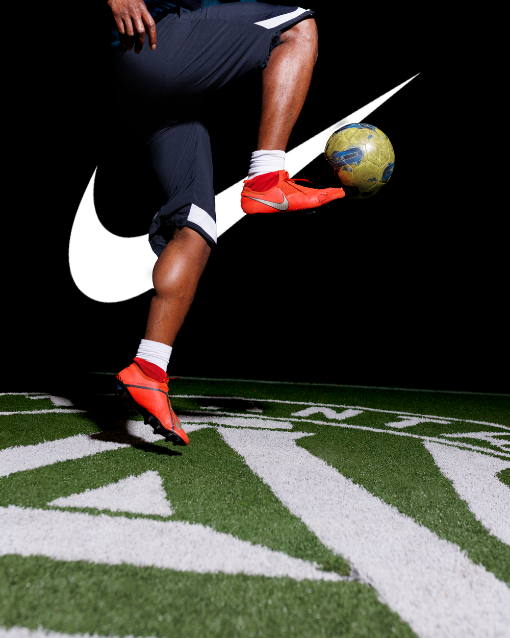 Nike soccer player juggling a ball in red cleats on turf with Nike swoosh logo.