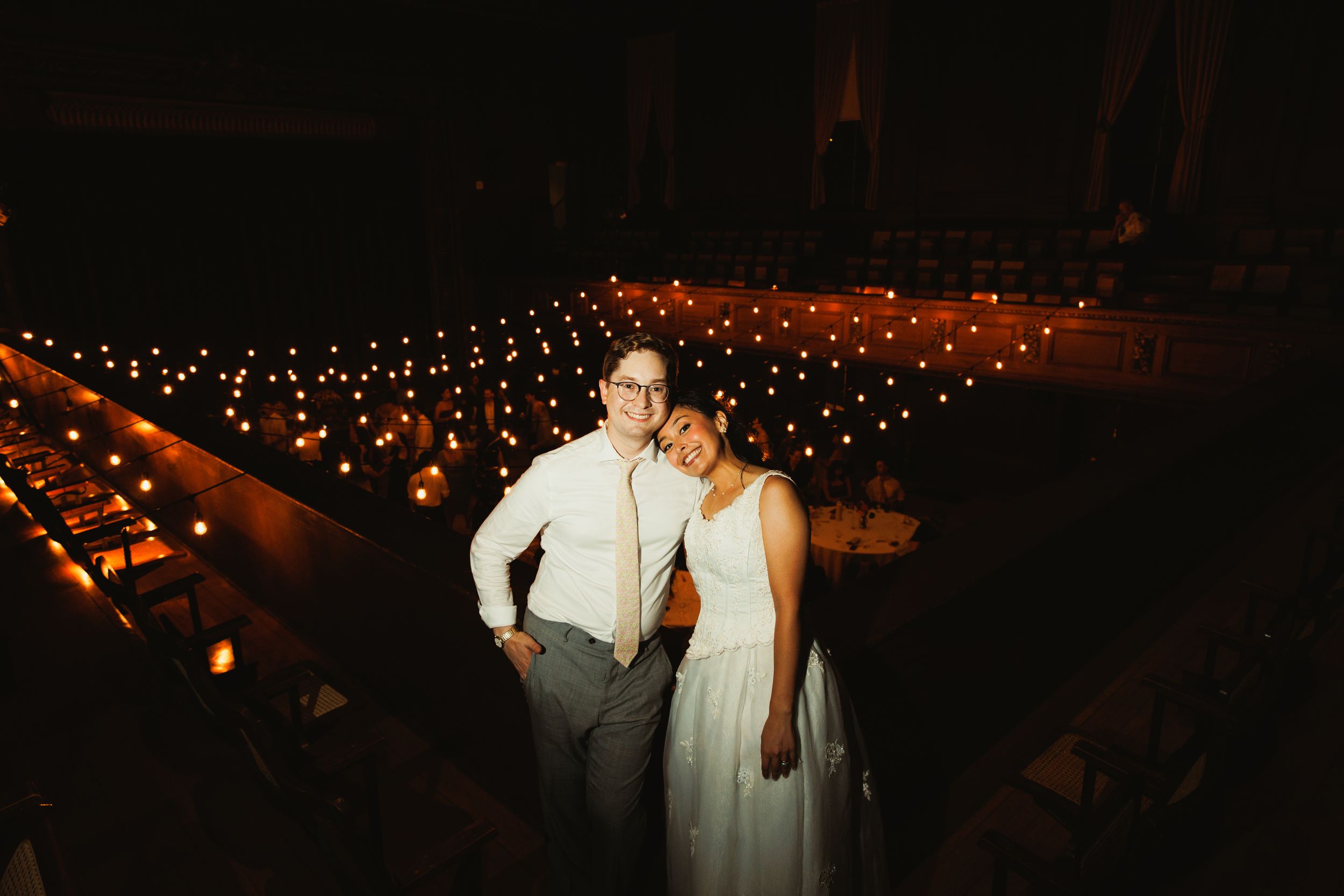 Couple posing under romantic string lights at nighttime wedding venue.