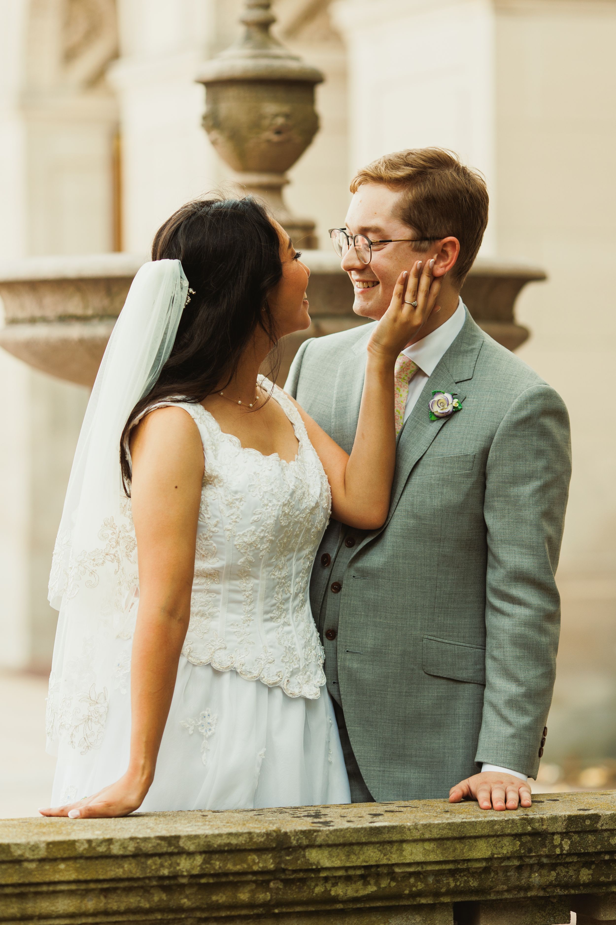 A romantic moment captured between a couple in wedding attire against a stone pillar.