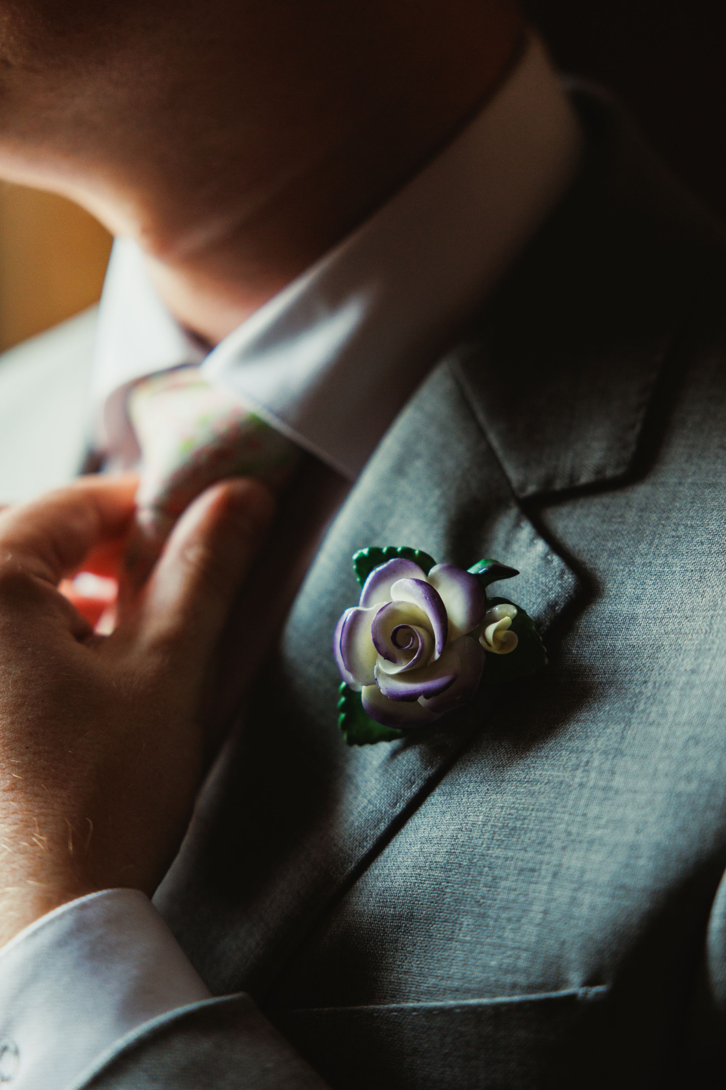 Close-up detail of purple rose boutonniere on grey suit jacket.