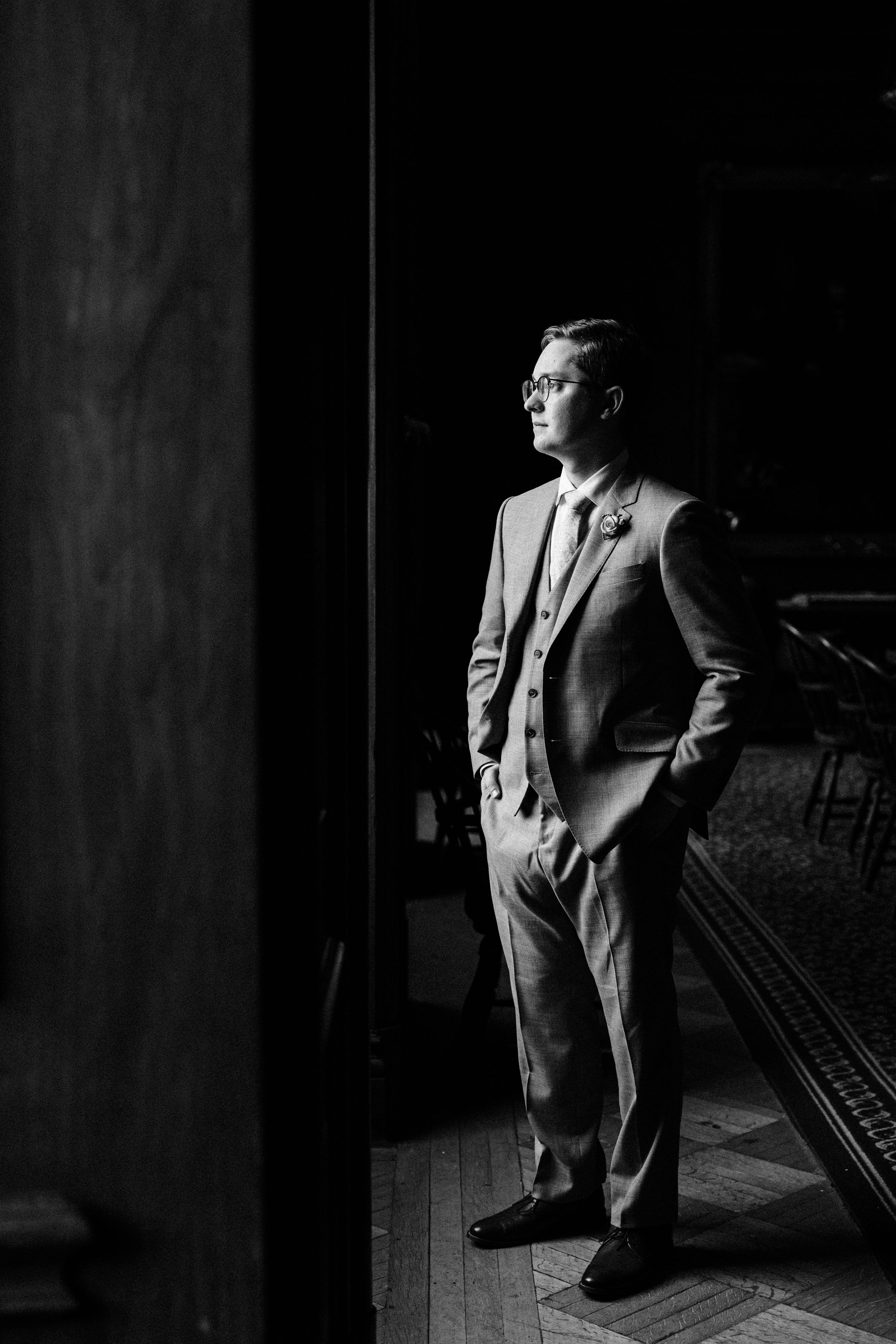Dramatic black and white portrait in formal attire near window light.