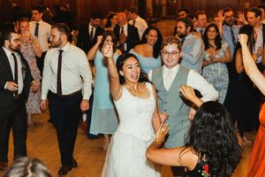 Wedding guests dance and celebrate on a crowded dance floor at an indoor reception.