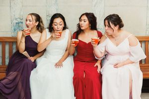 Bridesmaids in purple and red dresses share drinks and laughs during wedding celebrations.