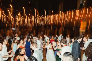 Wedding reception dance floor filled with guests dancing under warm string lights.