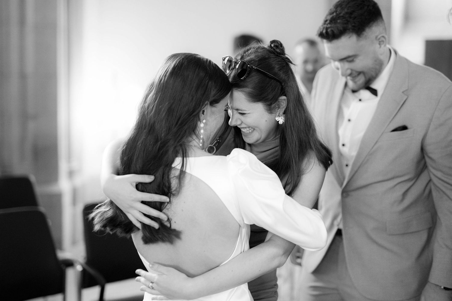 Black and white photo of a bride sharing a warm embrace with a smiling guest at a wedding celebration.