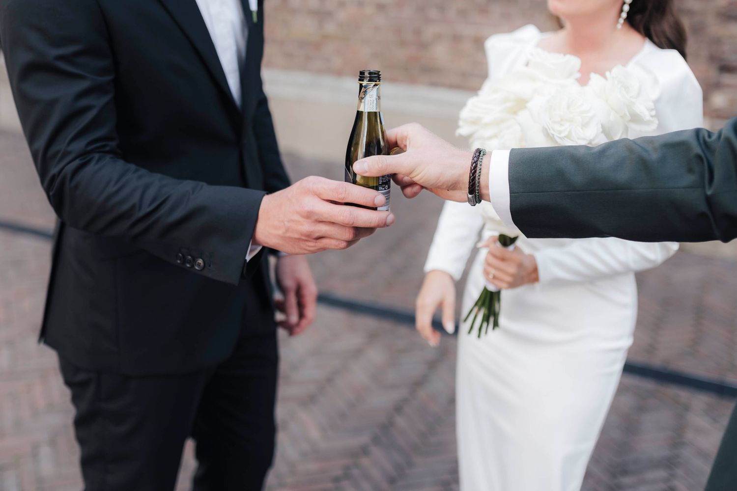 Bride and groom clinking beer bottles in celebration on their wedding day outdoors.