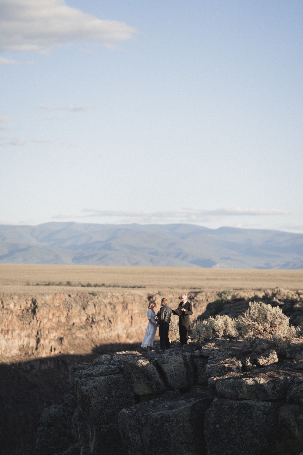 Small wedding ceremony on rocky cliff edge overlooking vast open plains and distant mountain range at Rio Grande Gorge in Taos New Mexico