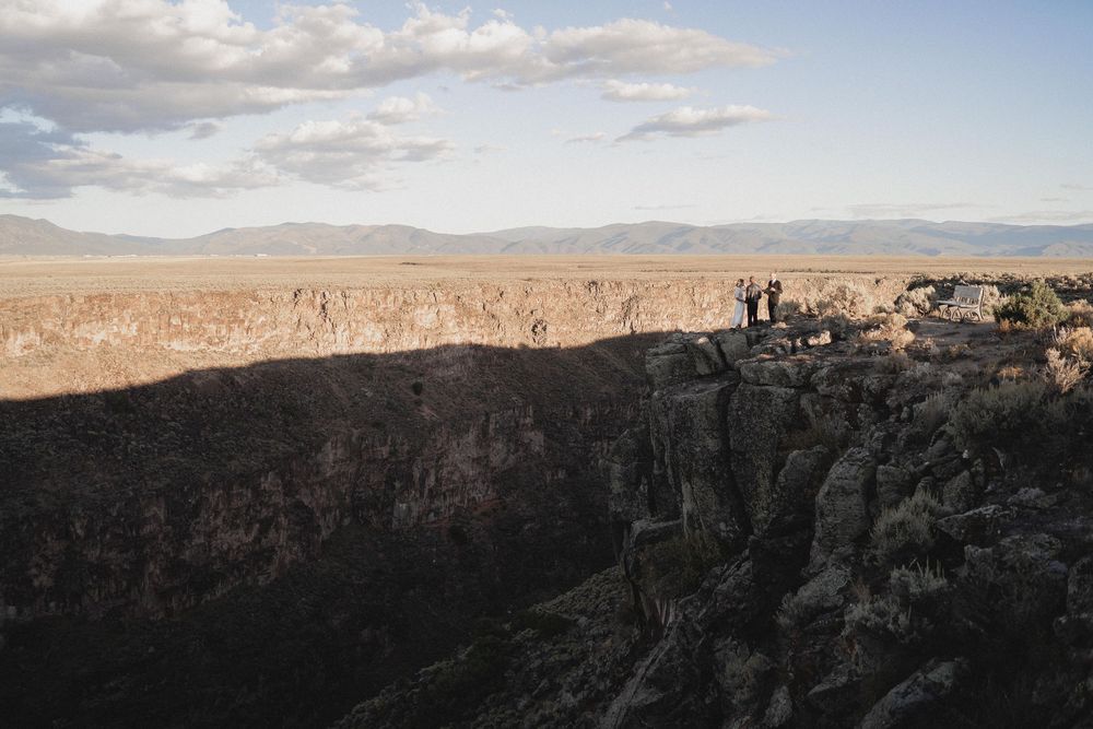 Tiny wedding elopement standing on dramatic rocky canyon edge with sweeping desert landscape at dusk at Rio Grande Gorge in Taos