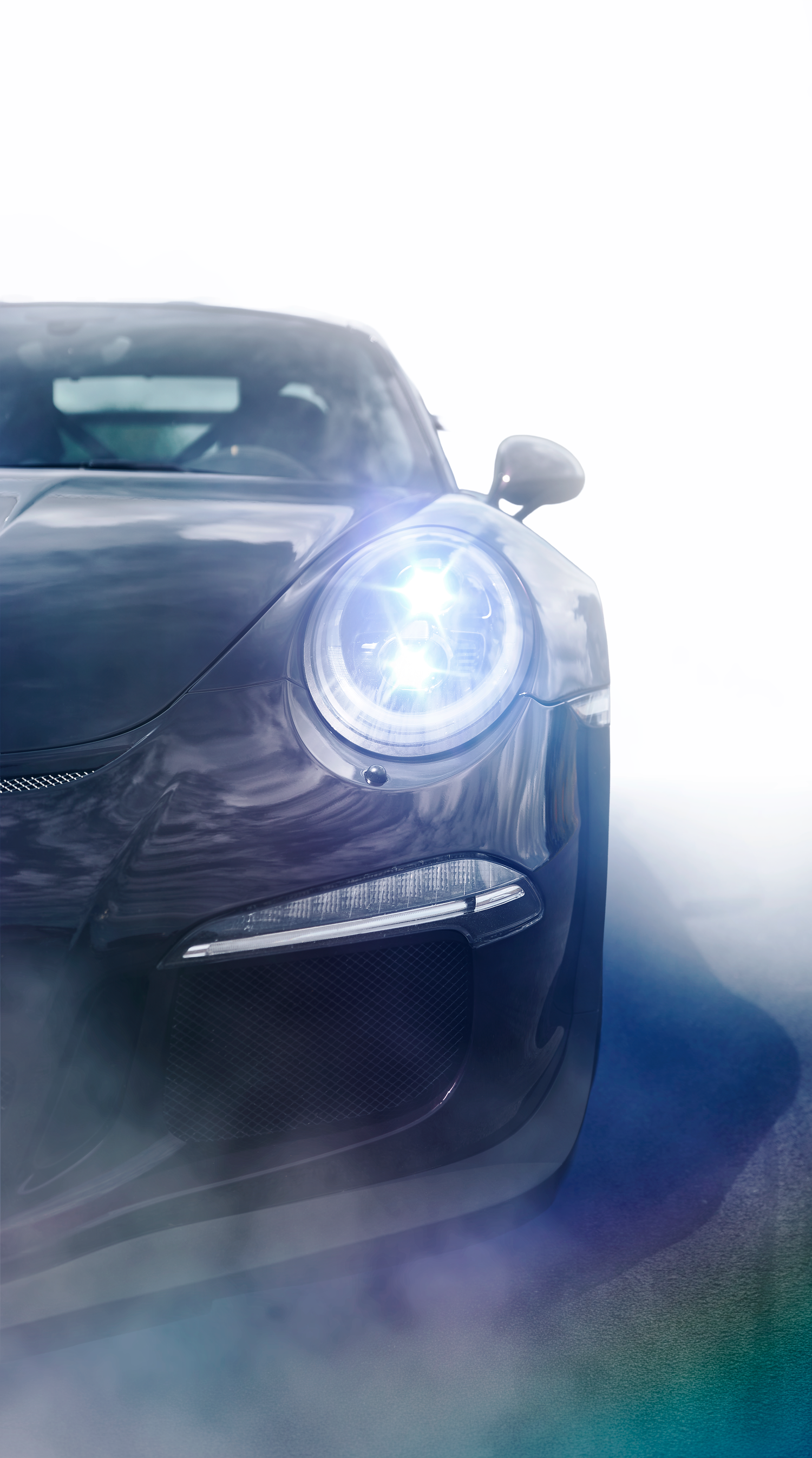 Close-up front view of a dark Porsche 911 GT3 with bright LED headlights glowing against a white background.
