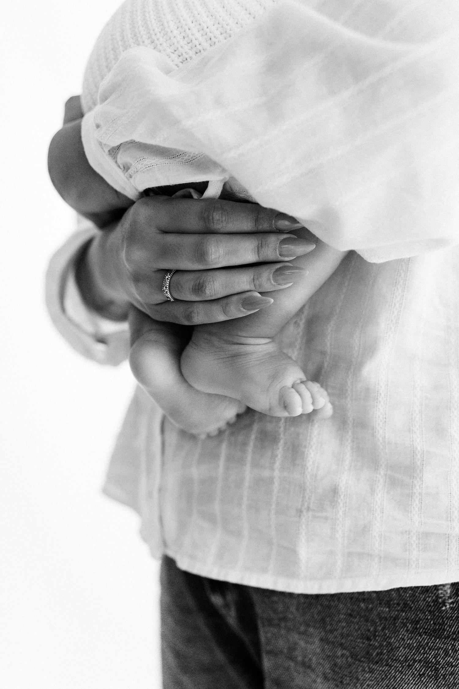 A laughing baby in a cream knit sweater being held by a mother in a bright white nursery chair.
