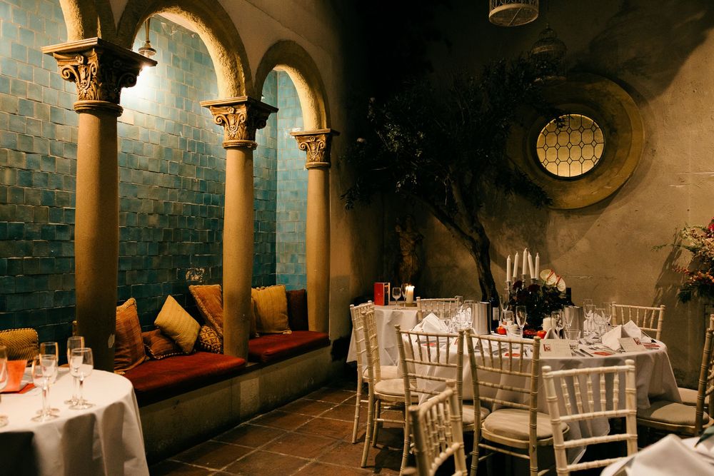 Elegant restaurant dining room with arched columns, teal tile walls, chiavari chairs, and candlelit tables set for a formal event.