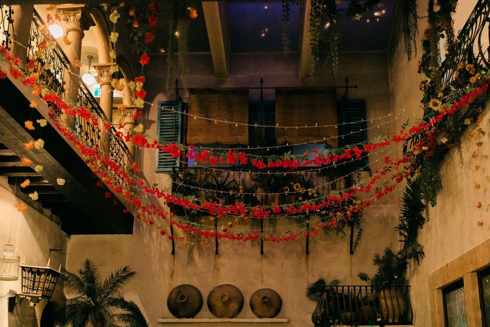 Festive indoor courtyard adorned with red floral garlands, string lights, and lush greenery on rustic balconies.