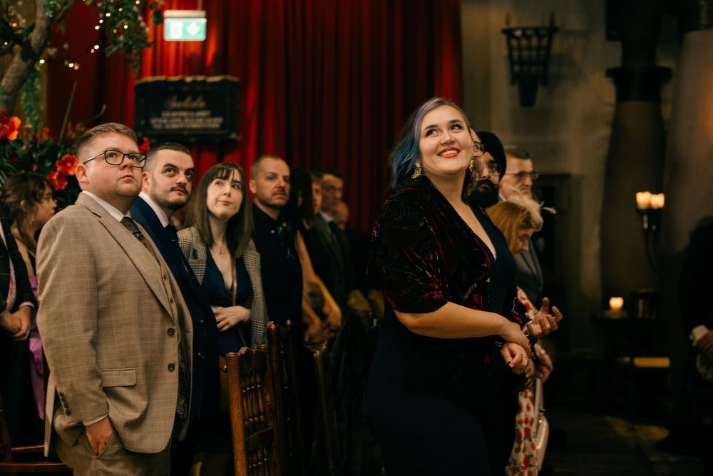 Guests in formal attire look upward in awe at an elegant evening event in a dimly lit venue.