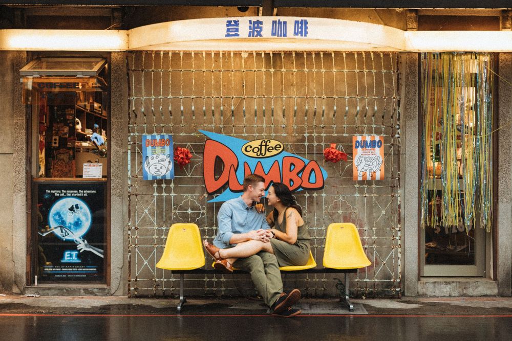 Couple sitting on yellow chairs outside a Dumbo coffee shop with Chinese signage in a romantic urban setting.