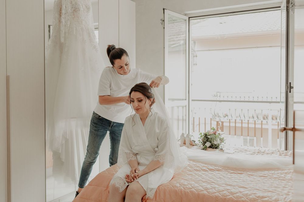 Preparativi della sposa nella stanza luminosa, accanto alla finestra aperta.