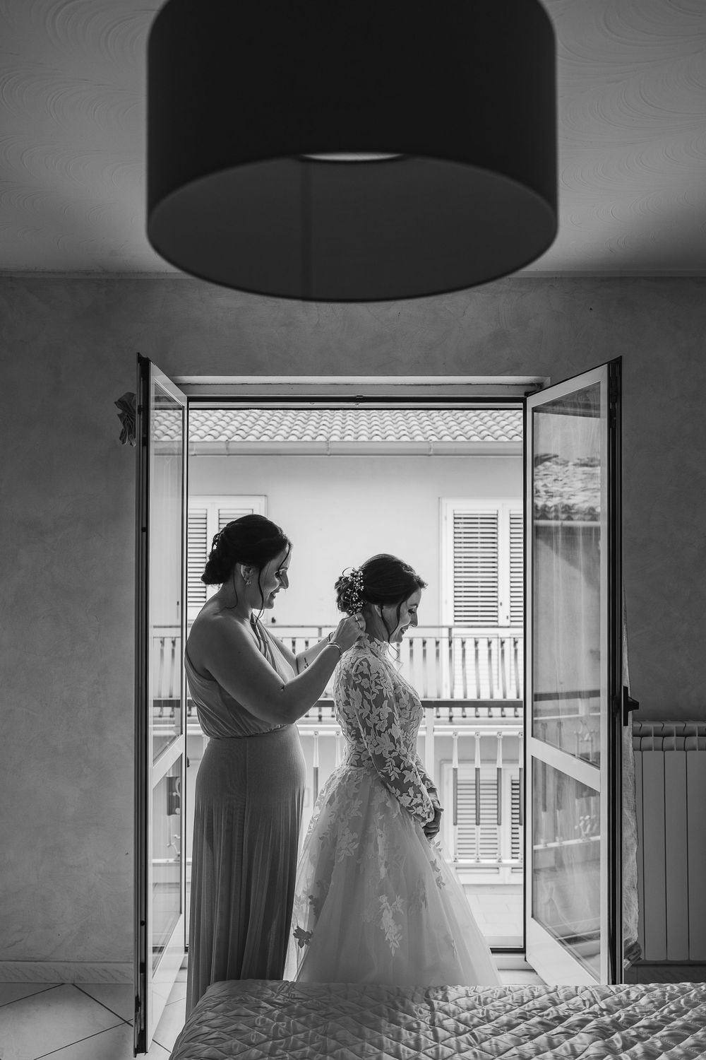 Due donne sistemano l’abito davanti alla finestra, in bianco e nero.