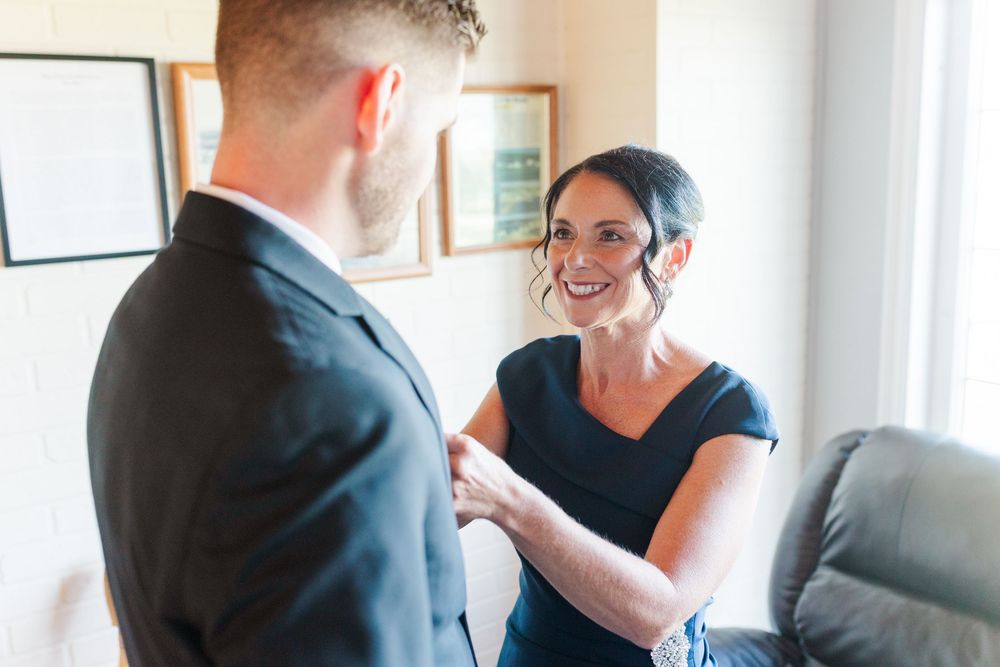 A smiling woman in a navy dress holds hands with a man in a black suit during a wedding ceremony indoors.