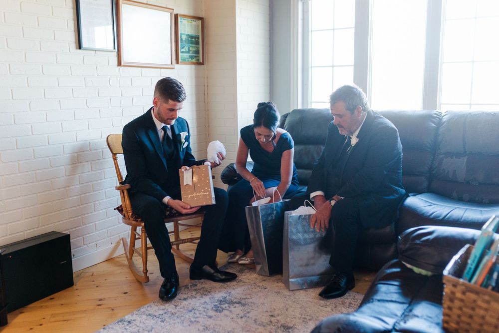 Three people in formal attire sit together in a living room, examining a wooden gift box during a wedding preparation.