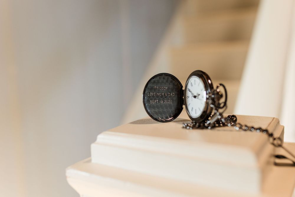 A vintage black pocket watch with engraved lid and chain resting on a white surface.