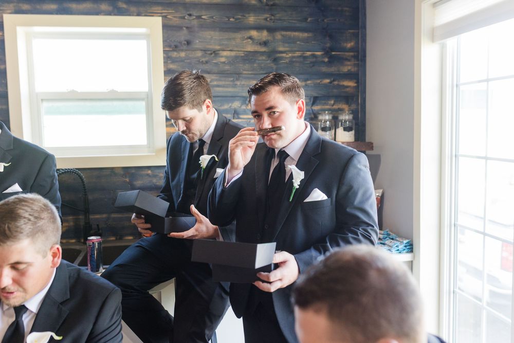Groomsmen in navy suits examining boutonnières before a wedding ceremony in a rustic venue.