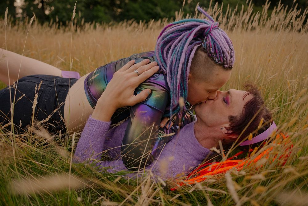 Two women sharing a romantic kiss while lying in a golden grass field outdoors.