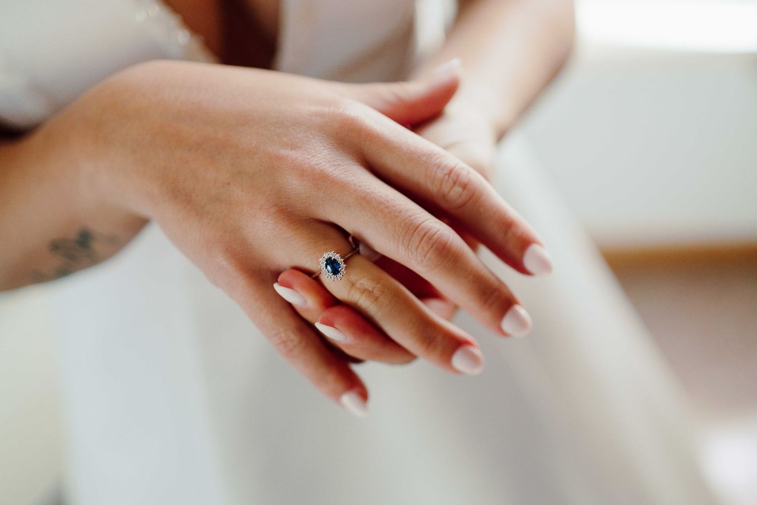 Close-up of a bride's hand wearing an elegant sapphire and diamond engagement ring with French manicure nails.