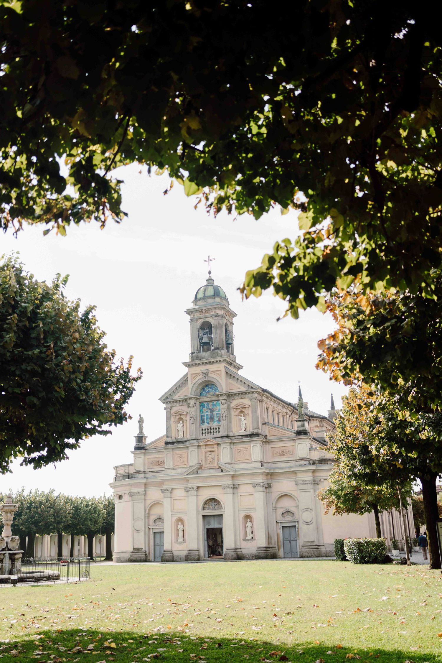 Historic baroque church facade framed by lush green trees on a sunny day.
