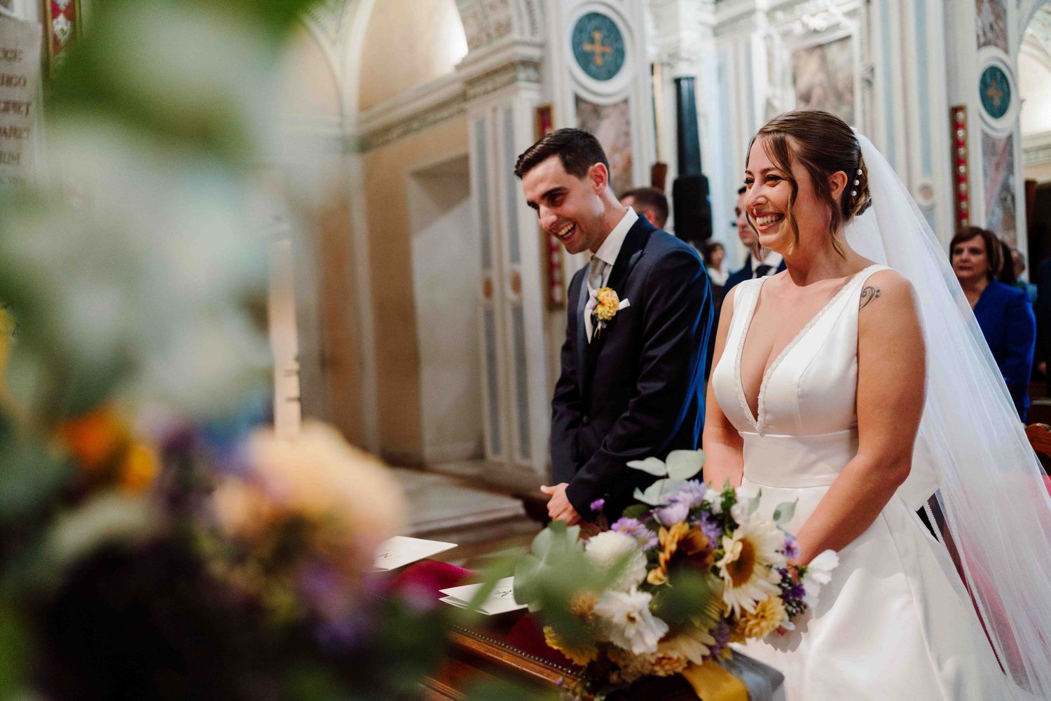 Bride and groom smiling joyfully at the altar of an ornate church during their wedding ceremony.