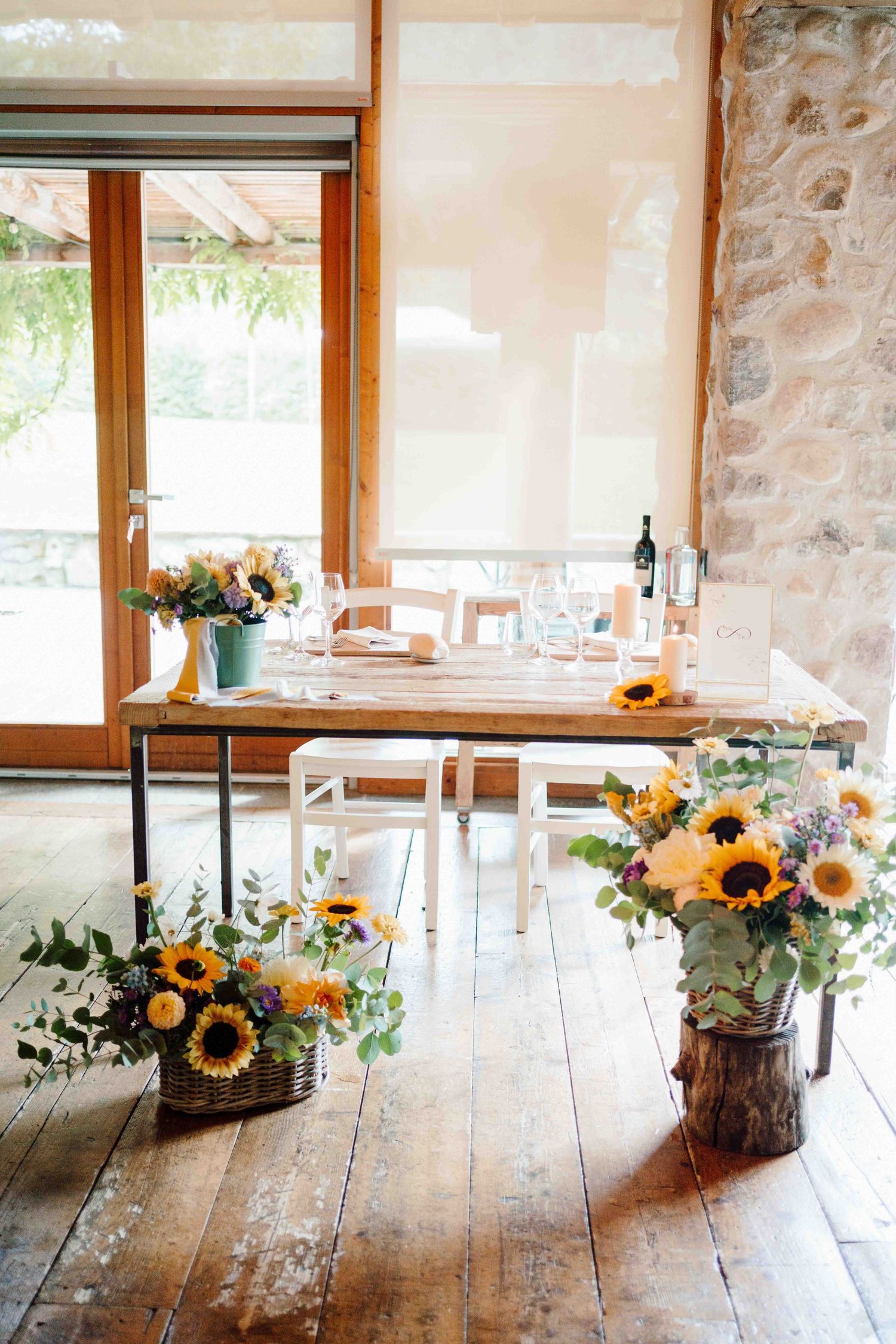 Rustic barn wedding venue with sunflower arrangements on wooden floor and decorated dining table with wine glasses.