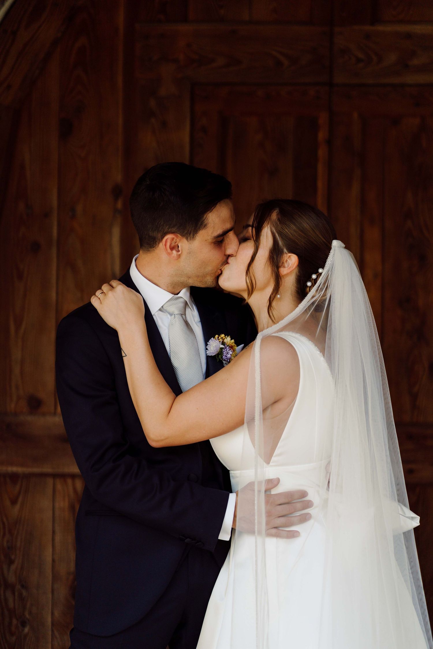 A bride and groom share a romantic kiss in front of a rustic wooden door on their wedding day.