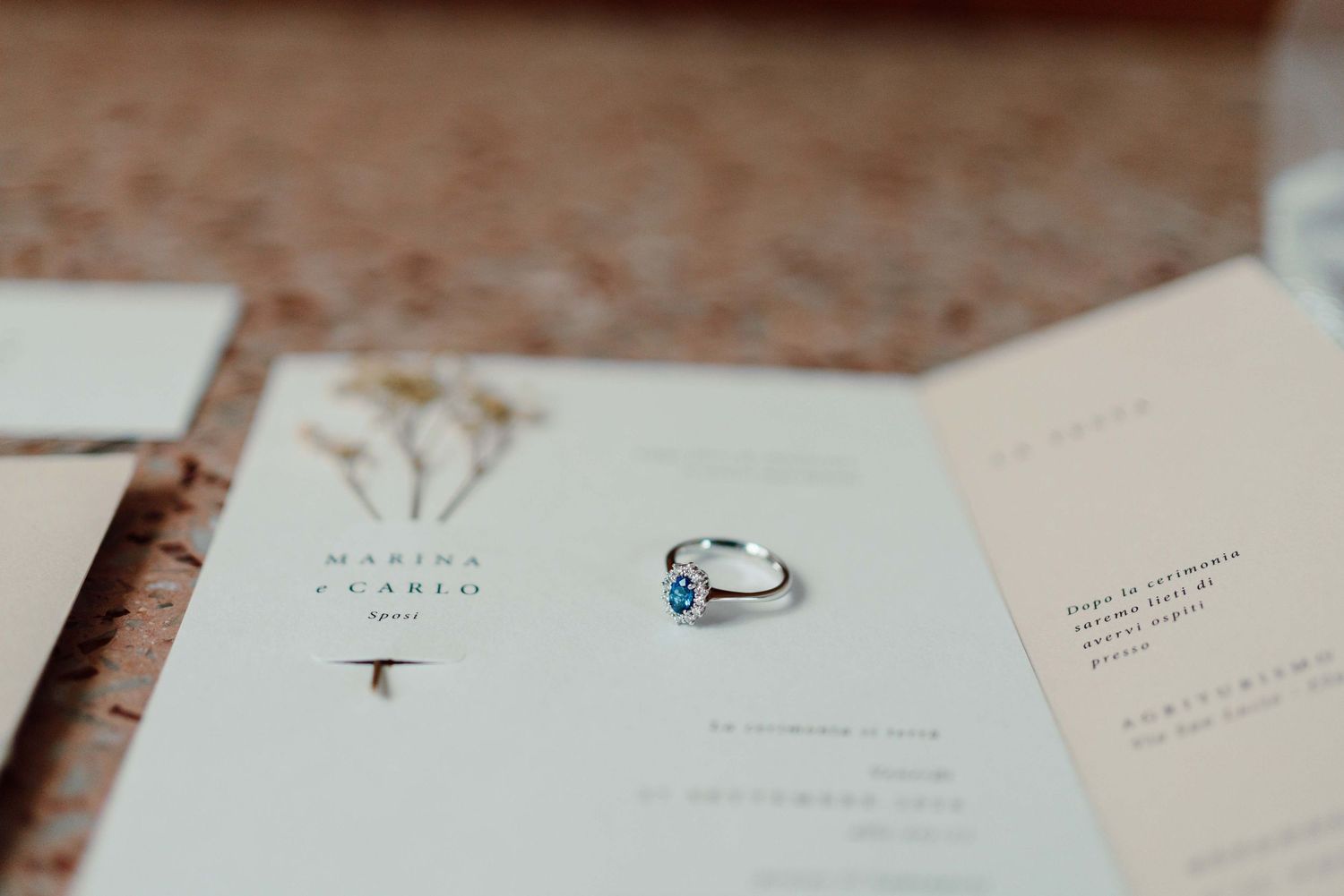 Silver ring with blue gemstone resting on elegant wedding stationery suite with floral accents.