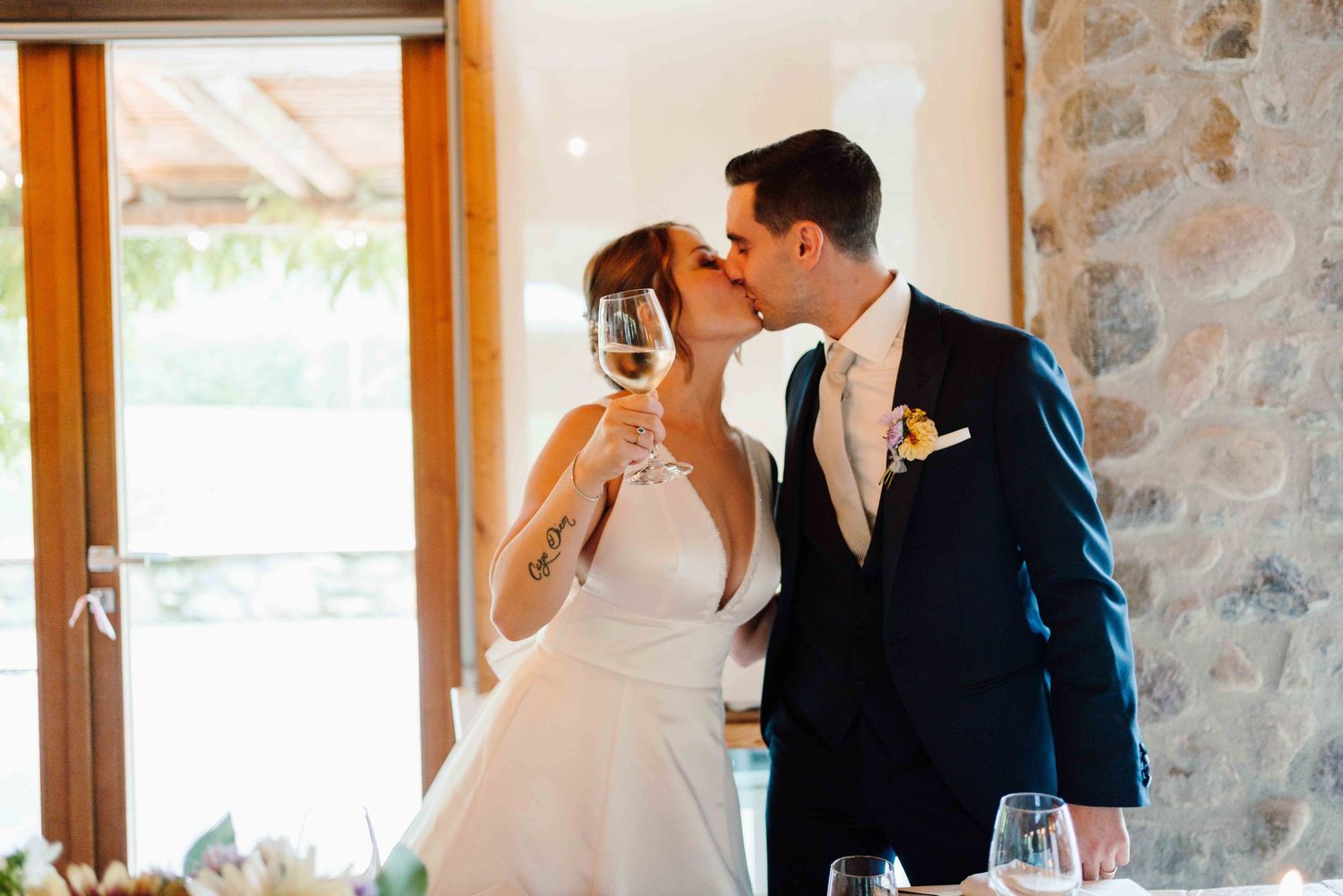 Bride and groom sharing a kiss while holding champagne glasses at their wedding reception venue.