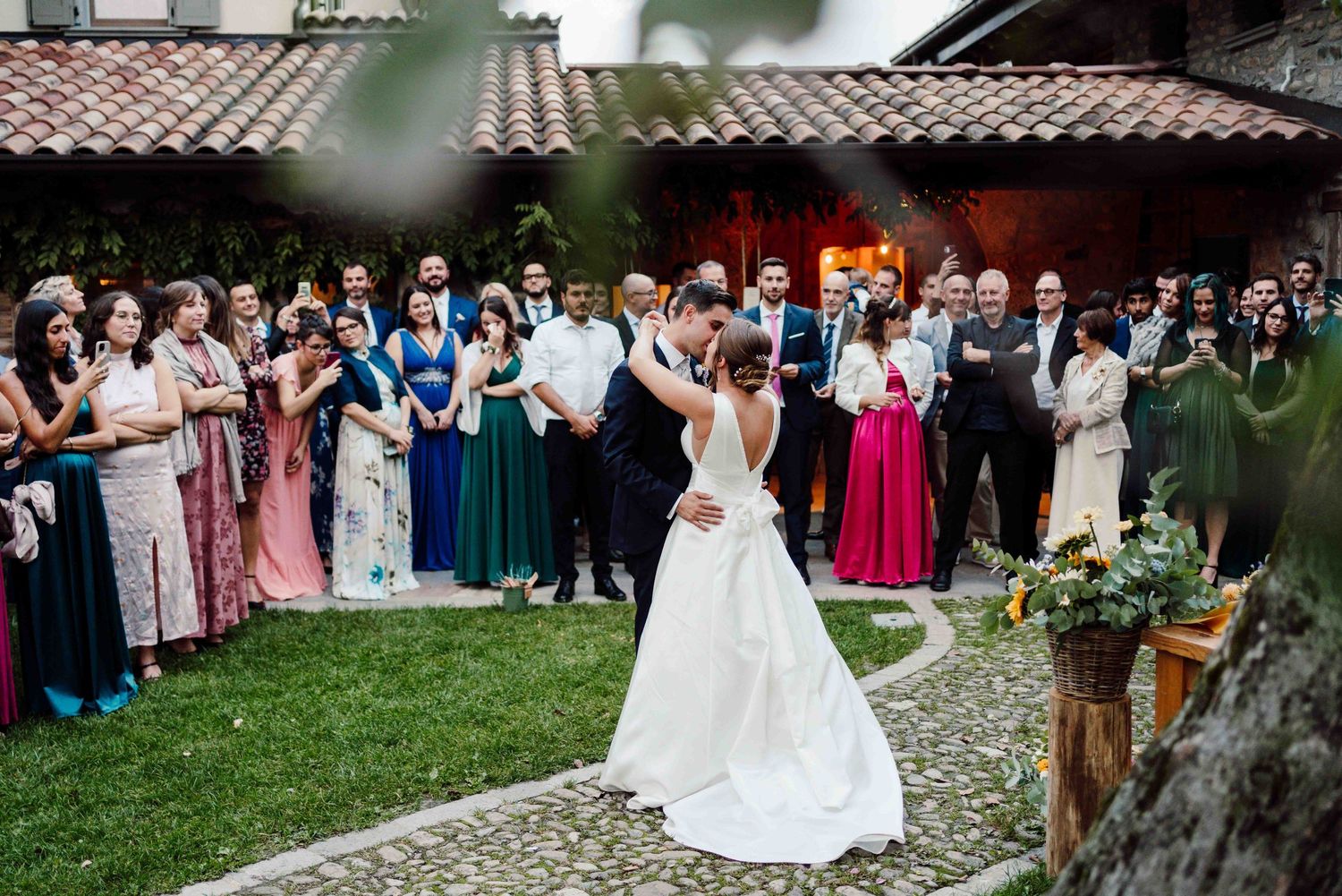 Bride and groom share first dance kiss at outdoor wedding reception with guests watching in courtyard.
