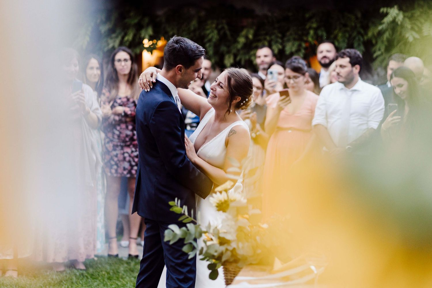 Bride and groom share first dance surrounded by wedding guests outdoors at romantic garden ceremony.