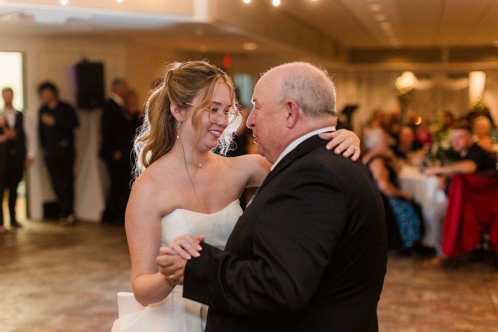 Bride in white strapless gown shares emotional father-daughter dance at elegant wedding reception.