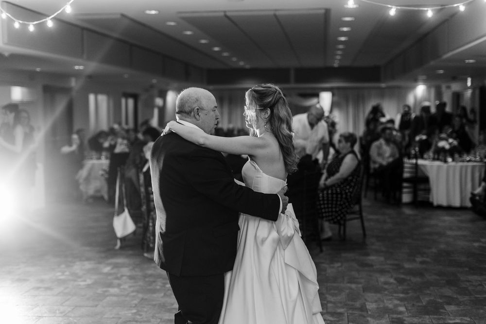 Black and white photo of a bride and her father sharing an emotional first dance at a wedding reception.