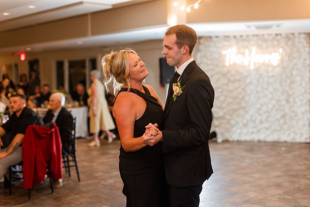 Mother and son share an emotional first dance at a wedding reception in a decorated ballroom.