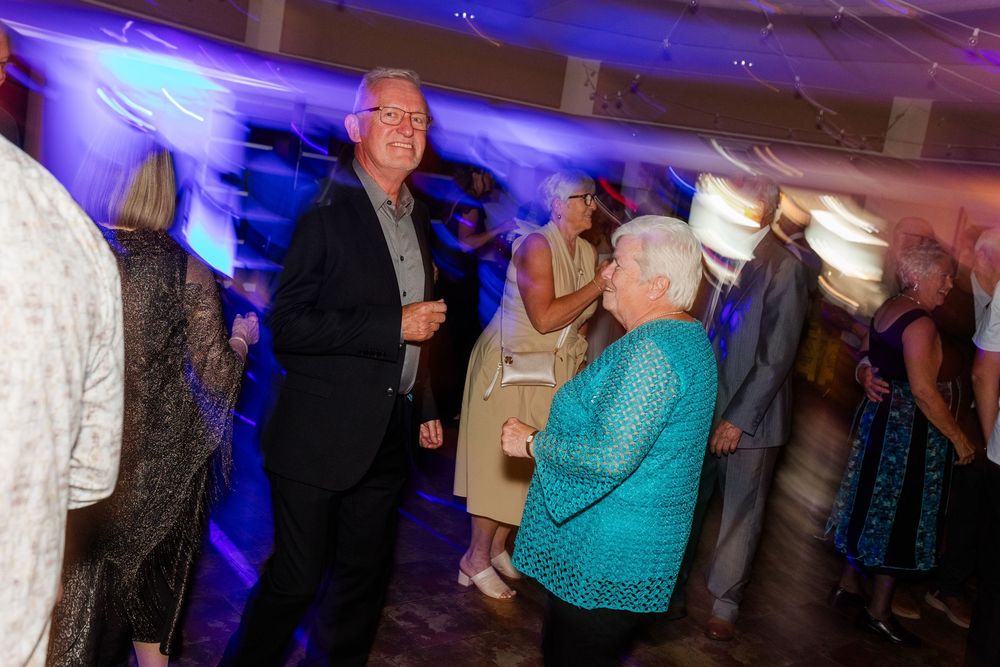 Elderly guests socializing and dancing at a formal evening event with blue and purple ambient lighting.