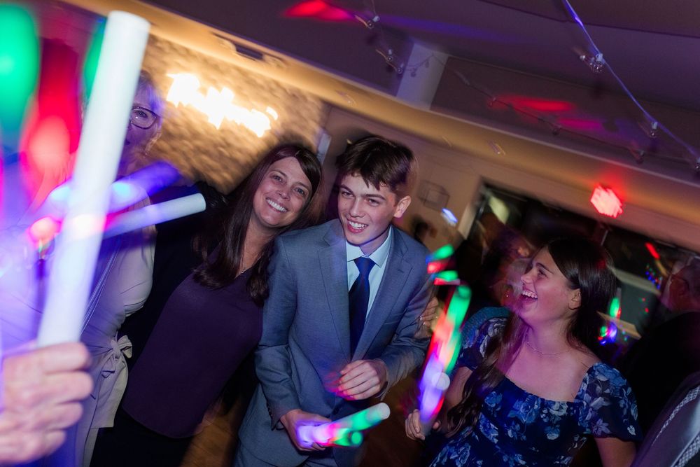 People dancing at a party with colorful glow sticks and festive lighting in a celebratory event.