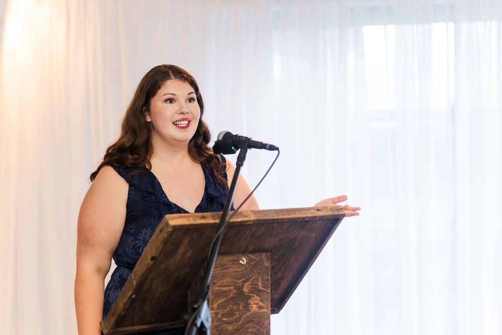 Woman in navy dress giving a speech at a wedding reception podium with microphone.
