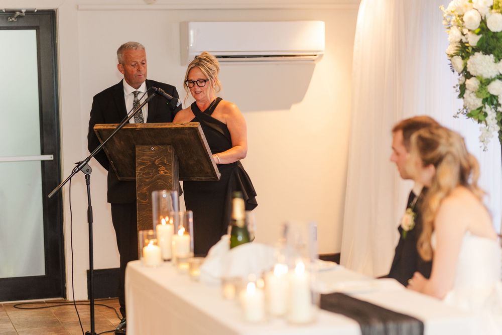 Elderly man and woman giving a speech at a wedding reception podium with candles and floral arrangements.